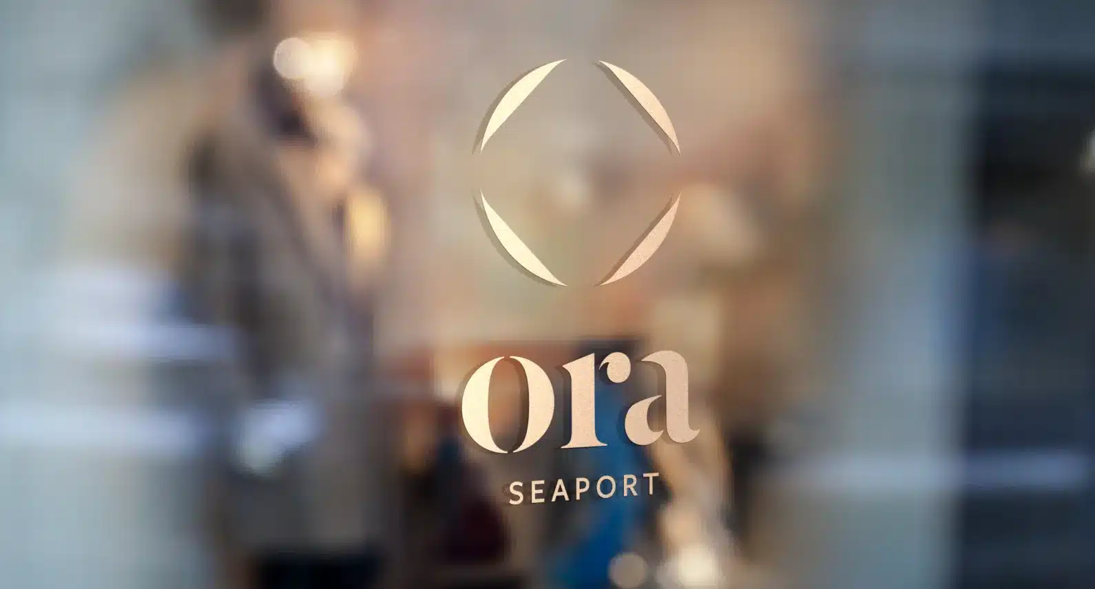 Ora Seaport logo on glass with blurred reflections of city lights and modern architecture