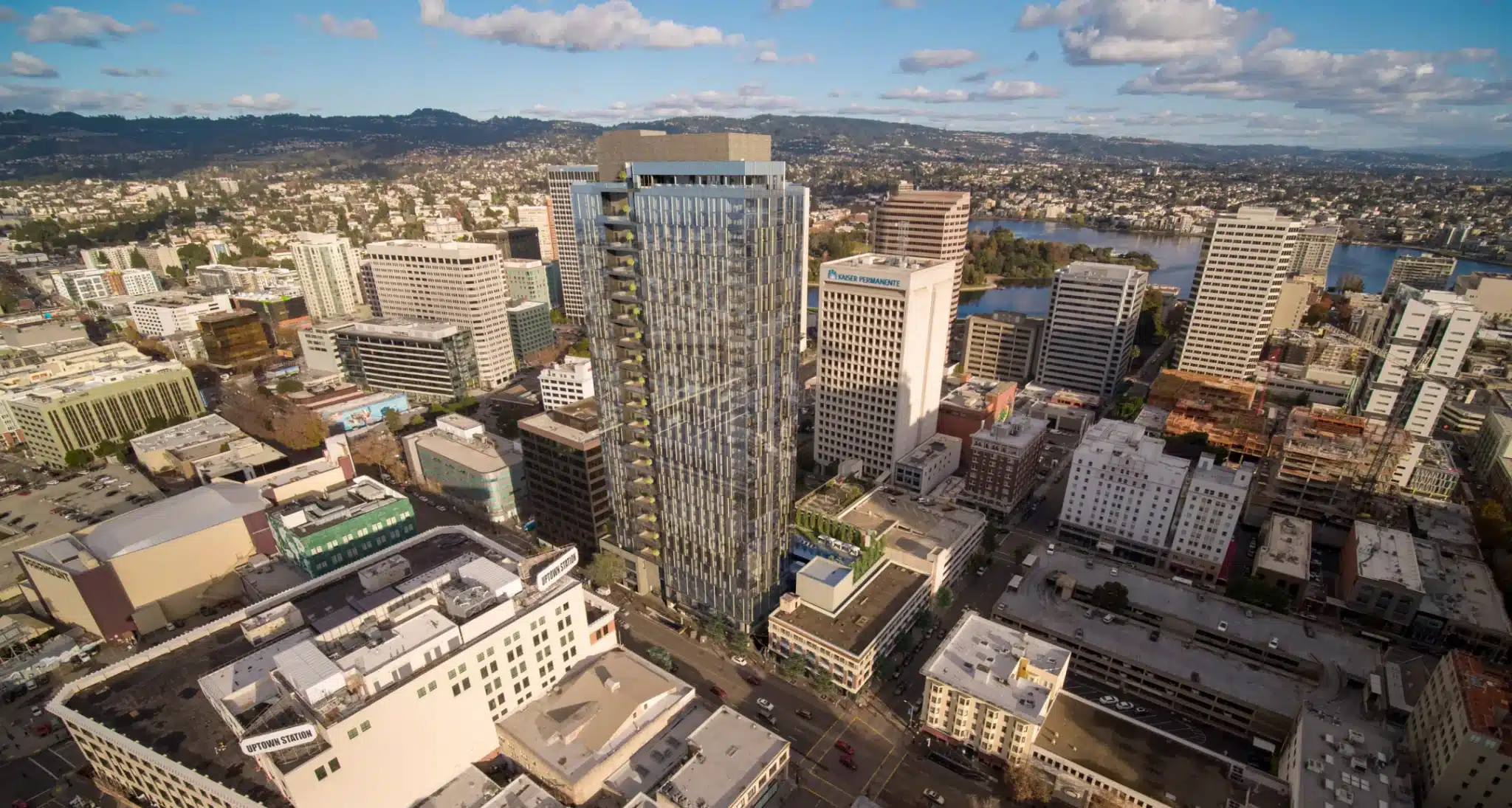 Aerial view of a glass high-rise surrounded by city buildings and a scenic mountain backdrop