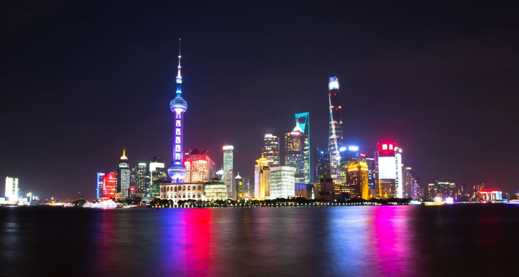 Vibrant night view of Shanghai skyline reflecting on water, featuring the Oriental Pearl Tower