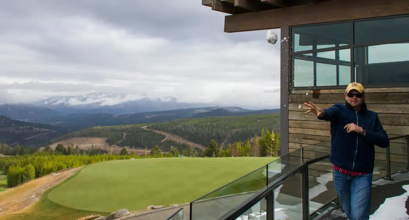 Man enjoying the mountain view from a modern balcony, tossing a snowball playfully