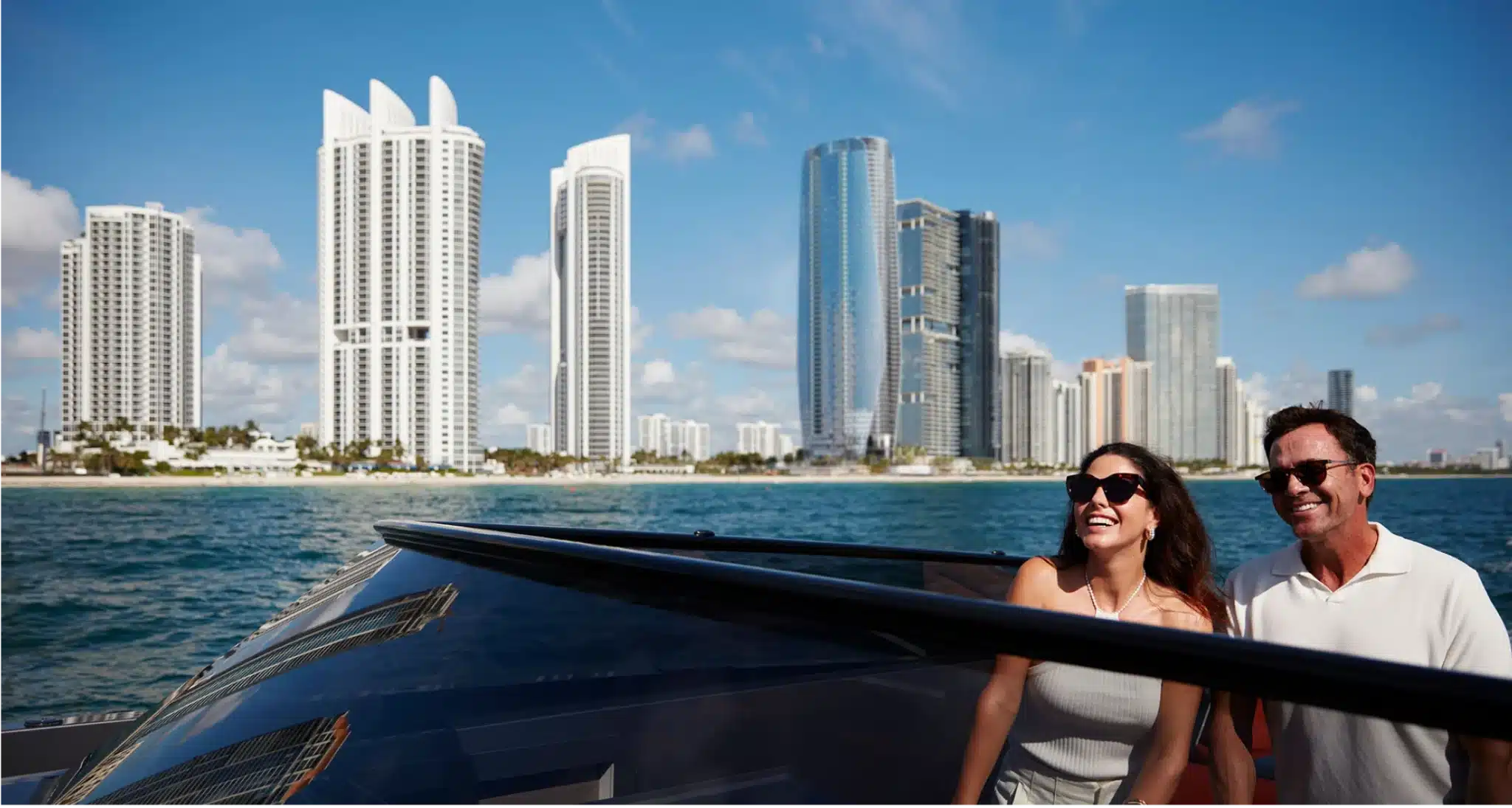 A couple enjoys a yacht ride with Miami’s luxury high-rises and blue ocean in the background